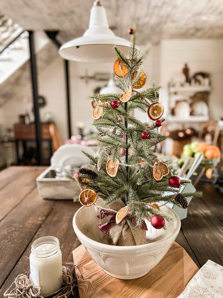 Large Vintage Bowl holds mini Christmas Tree with dried orange garland & red ornaments on Kitchen Island.  