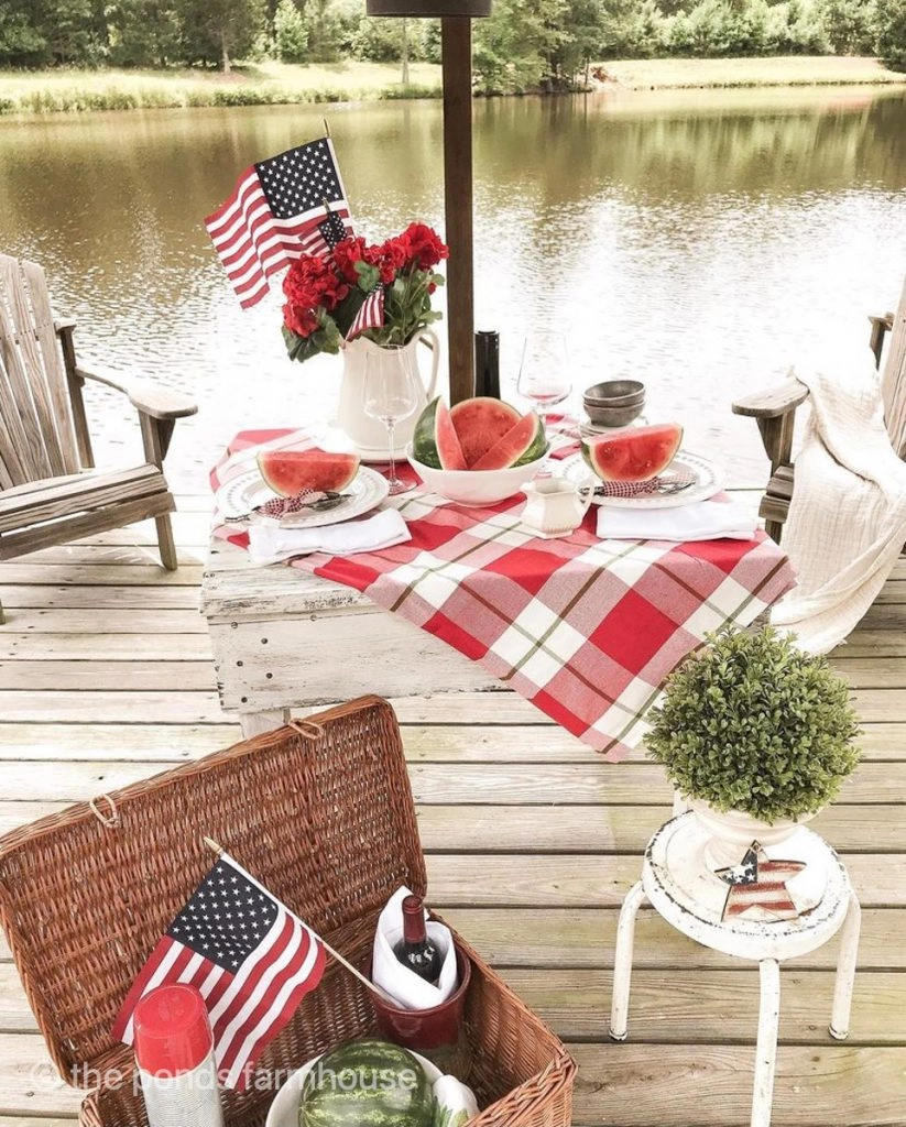 Red Geraniums in an ironstone white pitcher on table with watermelons for a pier picnic for Memorial Day.