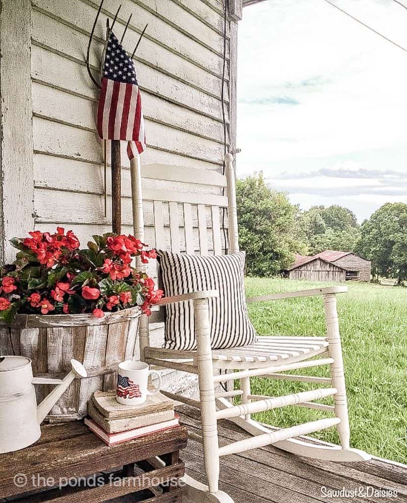 Country view with white rocker and American flag for patriotic decor on farmhouse.