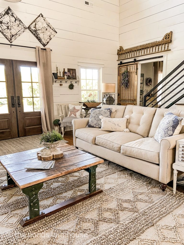 Country chic farmhouse living room with neutral sofa and repurposed coffee table, shiplap walls and vintage ceiling tiles.