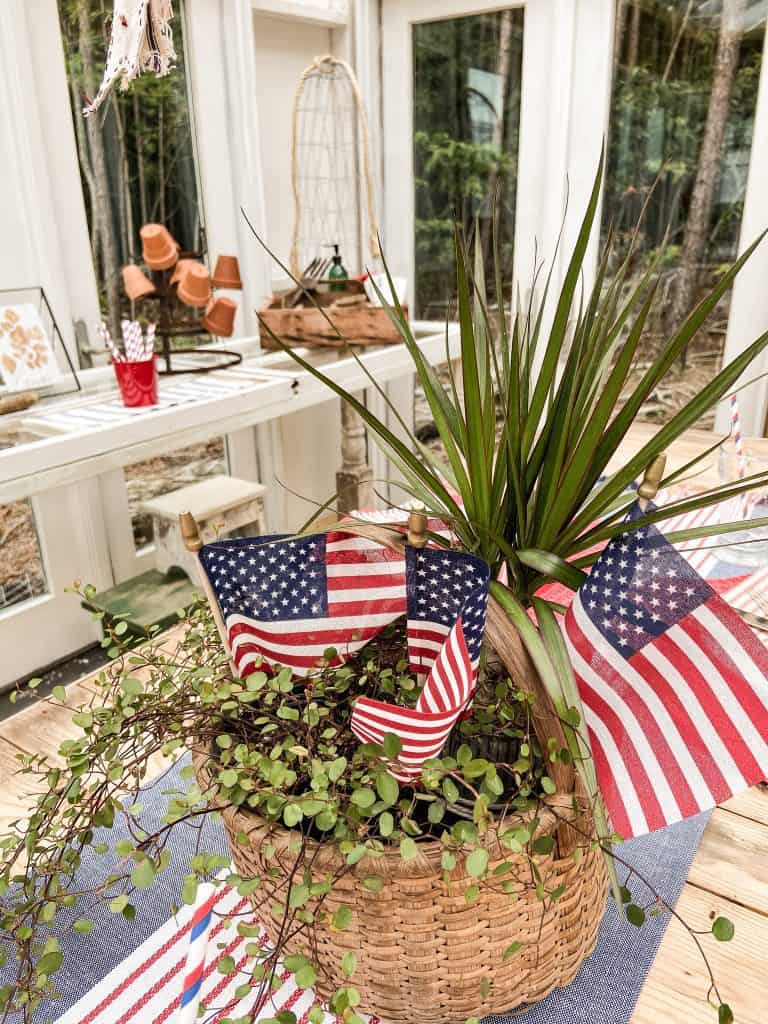 Thrift store basket filled with plants and dollar store flags make a great center piece for this casual Made Easy Patriotic Tablescape