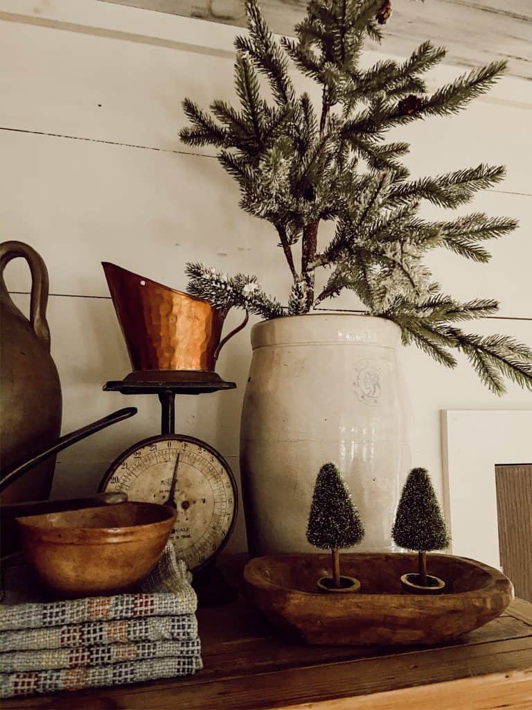 Vintage Crock filled with flocked mini Christmas Tree surrounded by vintage scale, copper, dough bowl and mini trees.