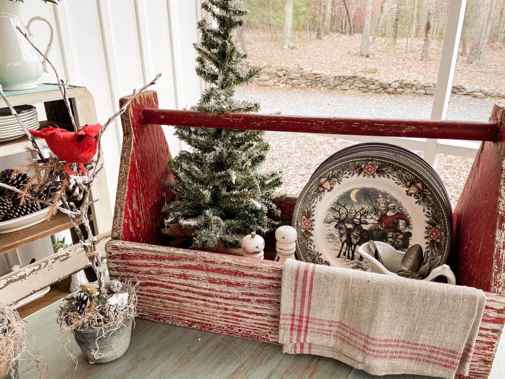 Vintage Red Tool Box holds mini Christmas Tree with Holiday Dinner Plates and vintage utensils on Screened Porch