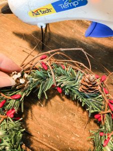 Hot glue mini pinecones to the DIY Christmas Candle Ring made from Dollar Tree supplies.