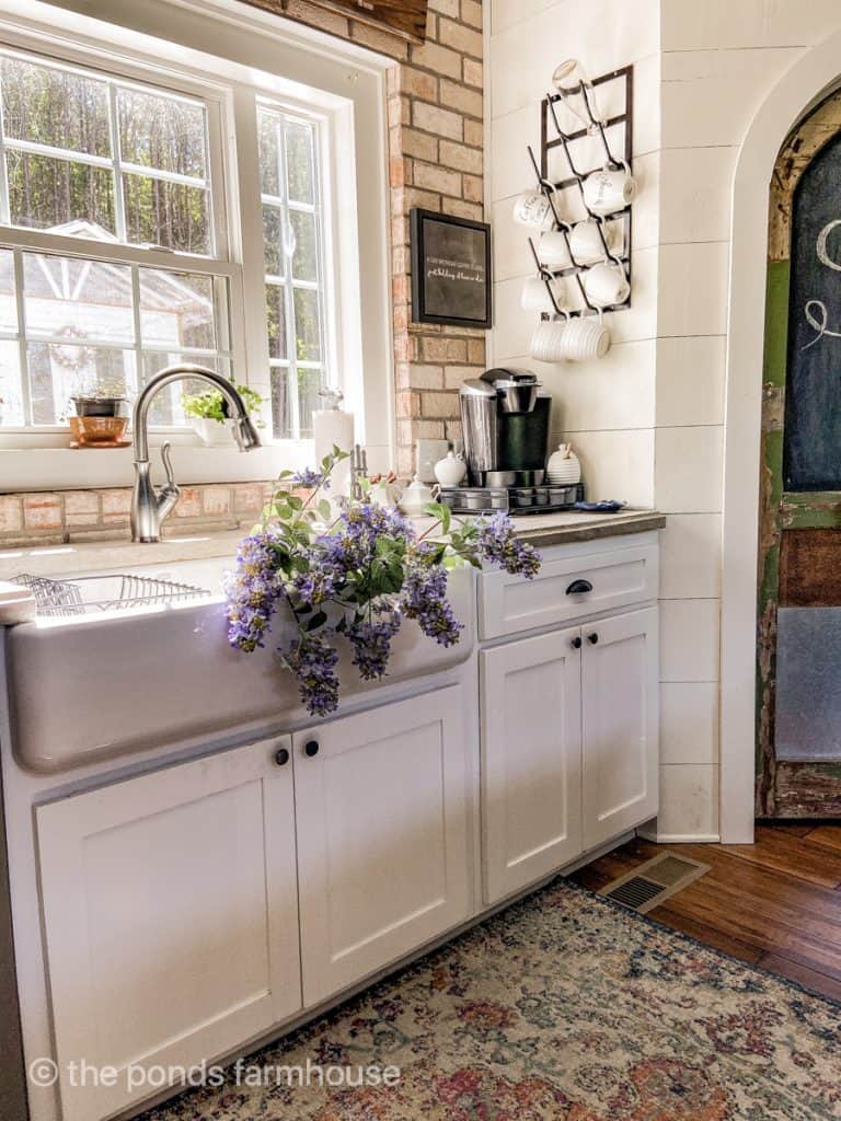 Farmhouse Style Kitchen with apron front sink, shiplap wall and brick backsplash.  Iron bottle drying rack.