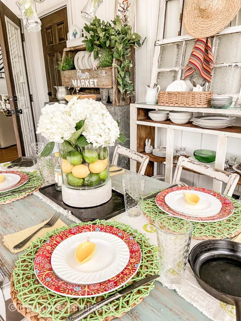 Cinco de mayo table decorations featuring green placemats and red floral chargers. Vase with lime, lemon, and hydrangeas. 