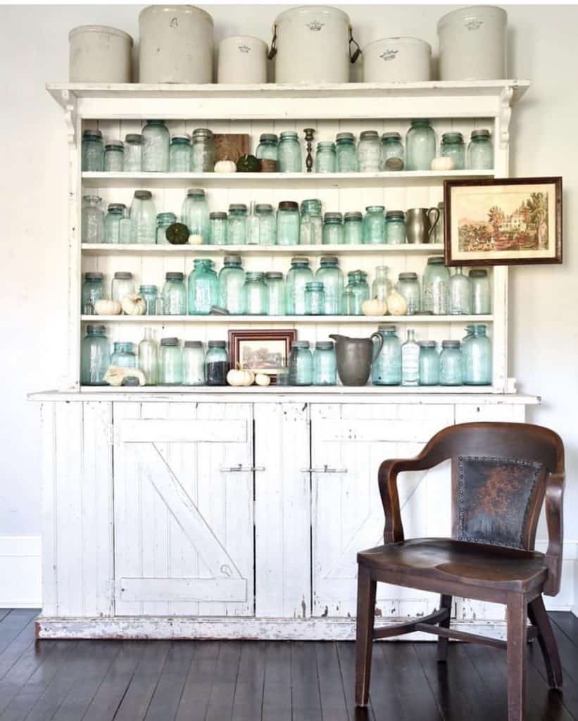 Open cabinet filled with collectibles of old blue mason jars, vintage crocks and art work.  