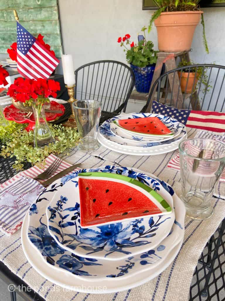 Outdoor Table with 4th of July theme table setting.  Watermelon slice plates, DIY Cutlery Patriotic Napkins and Blue and white diishes.  