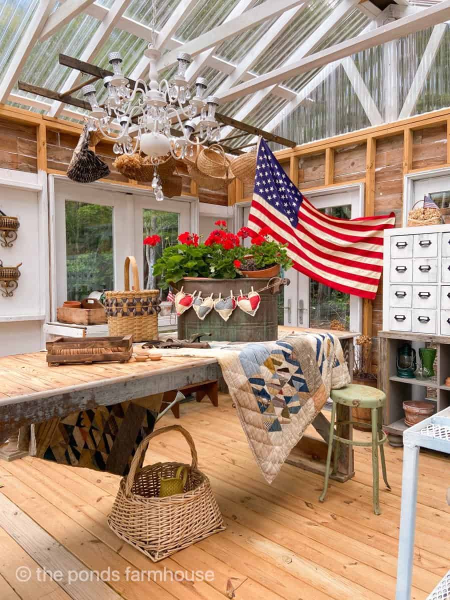 A vintage American Flag is the backdrop for the red geraniums and old quilt.  Patriotic 4th of July or Memorial Day.