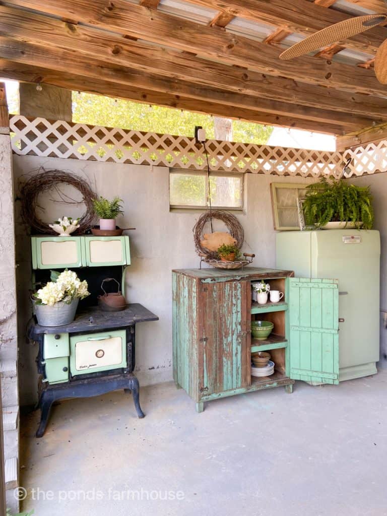 Vintage cookstove, antique primitive cabinet and antique refrigerator provide storage in outdoor kitchen.