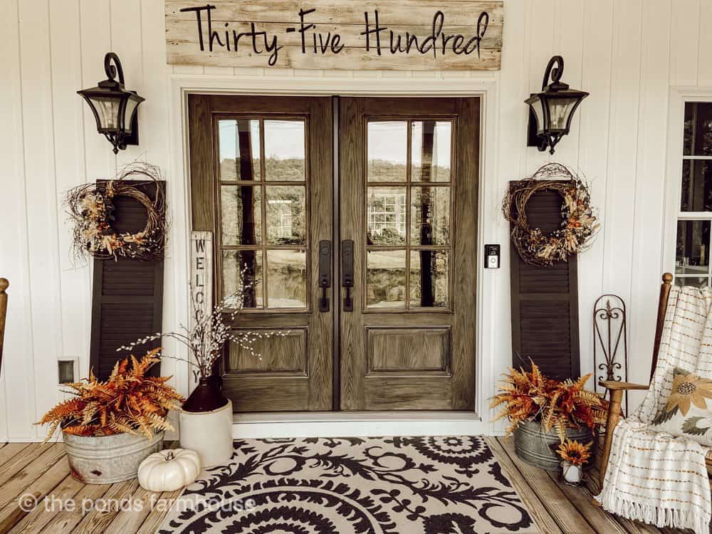 Front doors with large rug and black shutter with grapevine wreaths.  