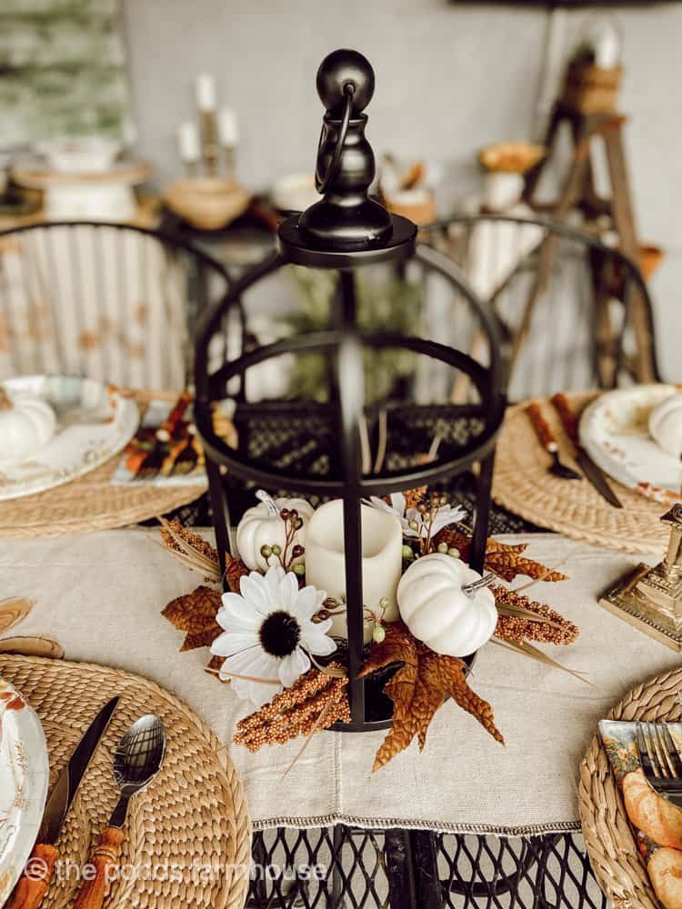 Lantern centerpiece for a fall dinner table in the outdoor kitchen.  Faux pumpkins and flowers surround a candle. 