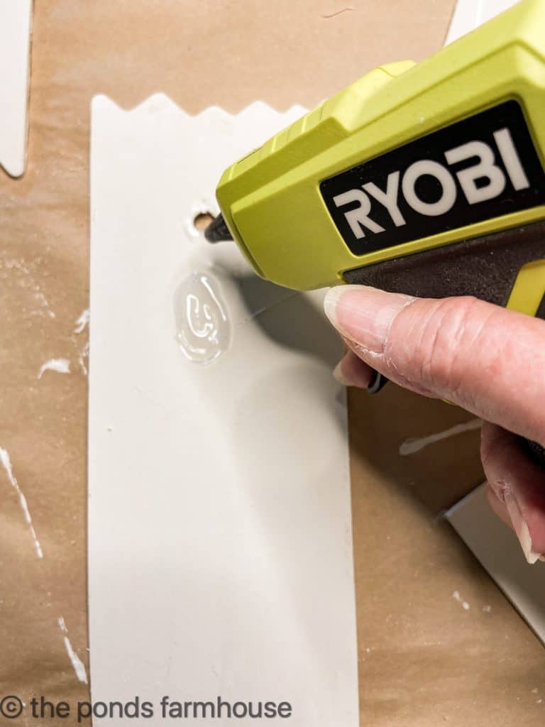 Creating an angel's face on a wooden board using hot glue for DIY Christmas Ornament.