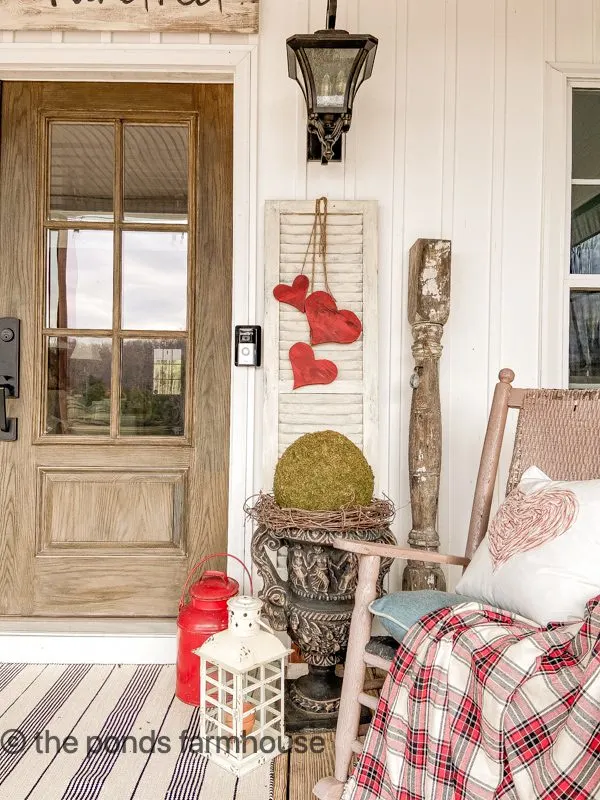 Cozy Winter Porch ideas with plaid blankets, rocking chair and wooden heart swag on white shutter.  