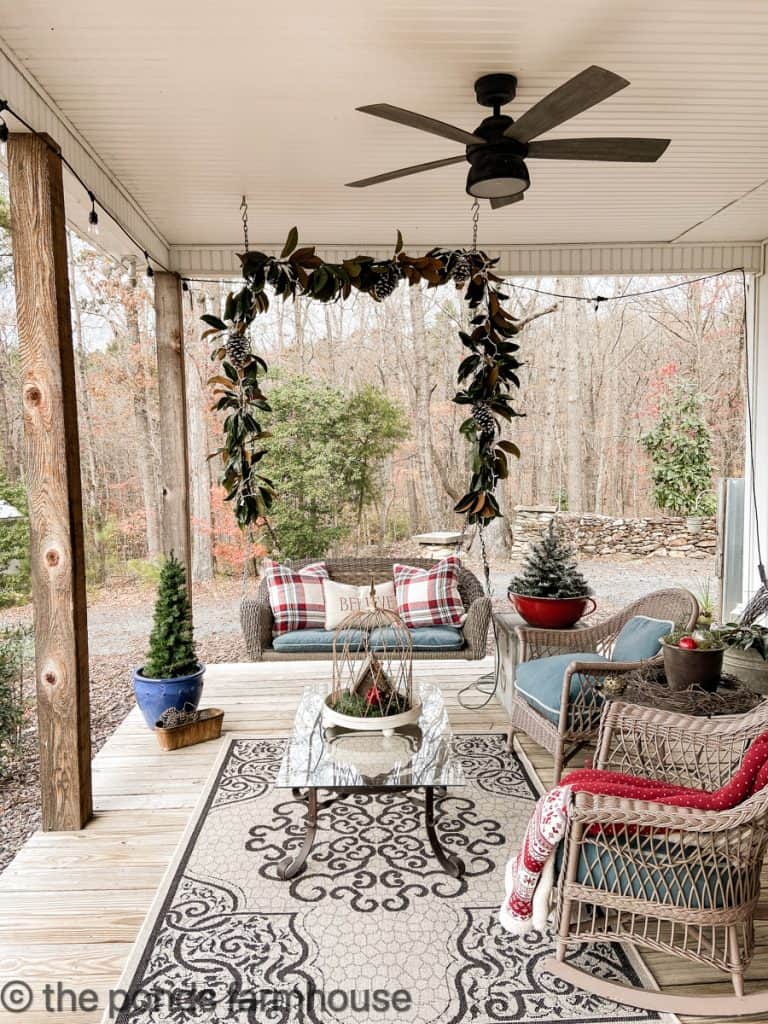 Farmhouse Christmas decorated porches with swing and magnolia garland and wicker seating area.