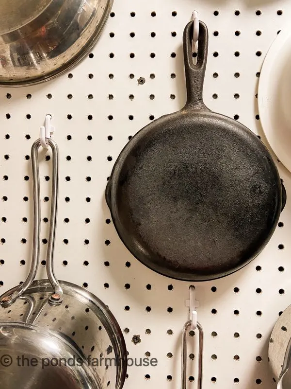 Pots and pans hanging on peg board wall.
