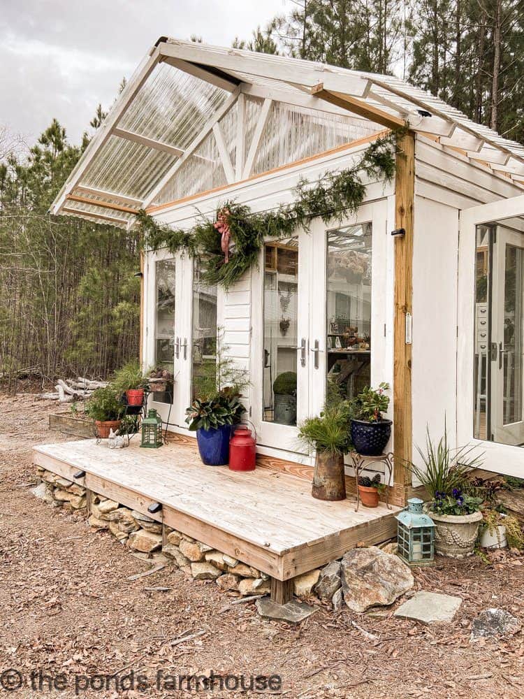DIY Greenhouse Decorated for Christmas - DIY She Shed with a porch and real cedar garland and wreath.