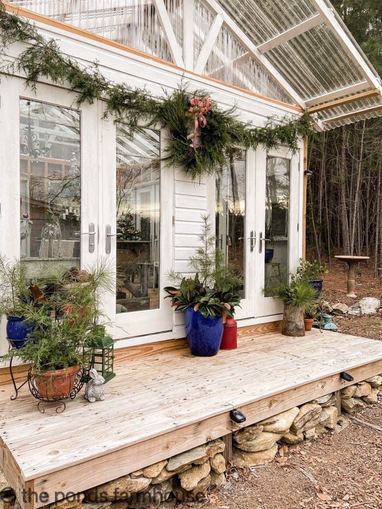 Christmas Cedar Garland on the DIY Greenhouse with Fresh evergreens on the porch.