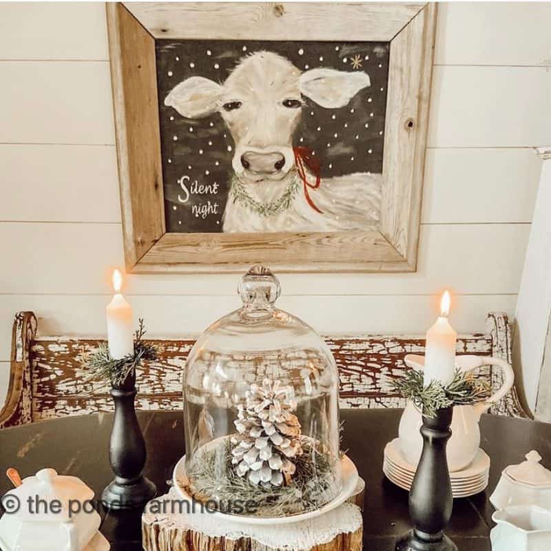 Silent Night Painting with cloche over a snowy pinecone and black candlesticks with ironstone table decorations for winter.