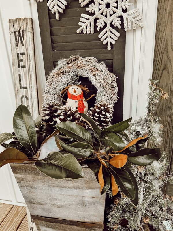Magnolia leaves and foraged pinecones, snowy wreath and snowman in planters for winter on front porch