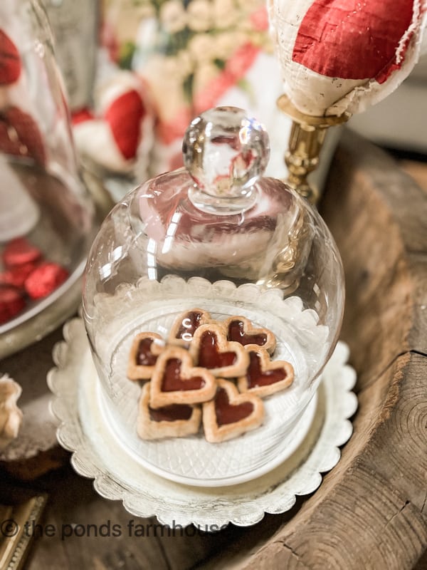 Cookies under a glass dome sitting on a white plate.