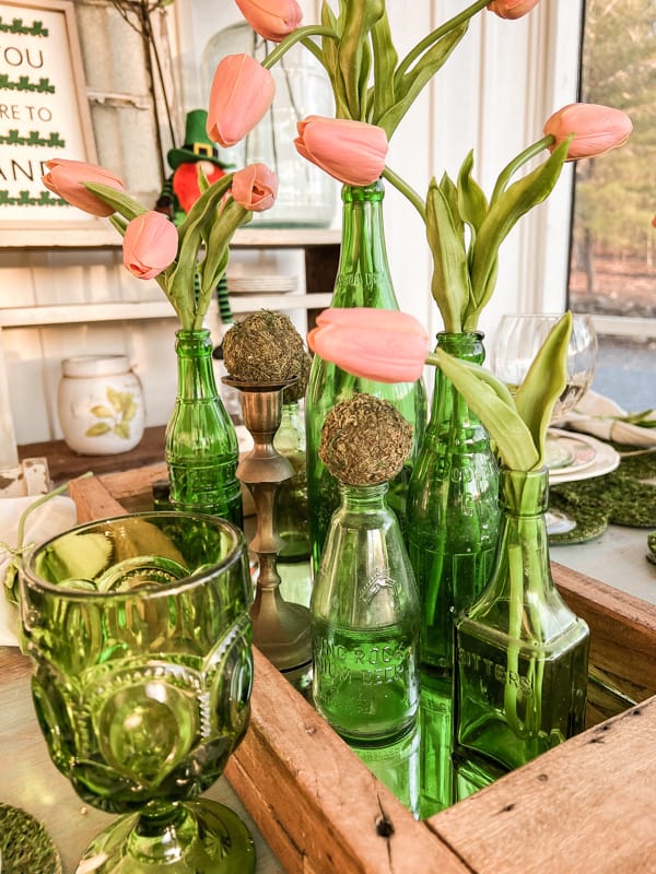 St. Patty's Day Tablescape with Tulips in vintage drink bottles sitting in wooden crate. Vintage green glasses.