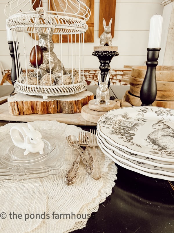 Decorating a Table for Easter with Easter bunny in cage and wooden riser Easter table setting. Black and White dishes & bunny napkin rings