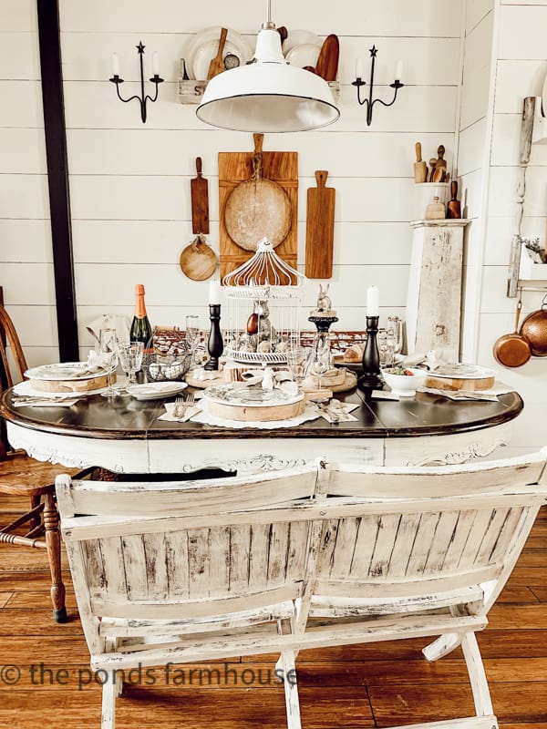 Dining table filled with thrift store finds including candlesticks, bread boards, ironstone, and other vintage pieces.