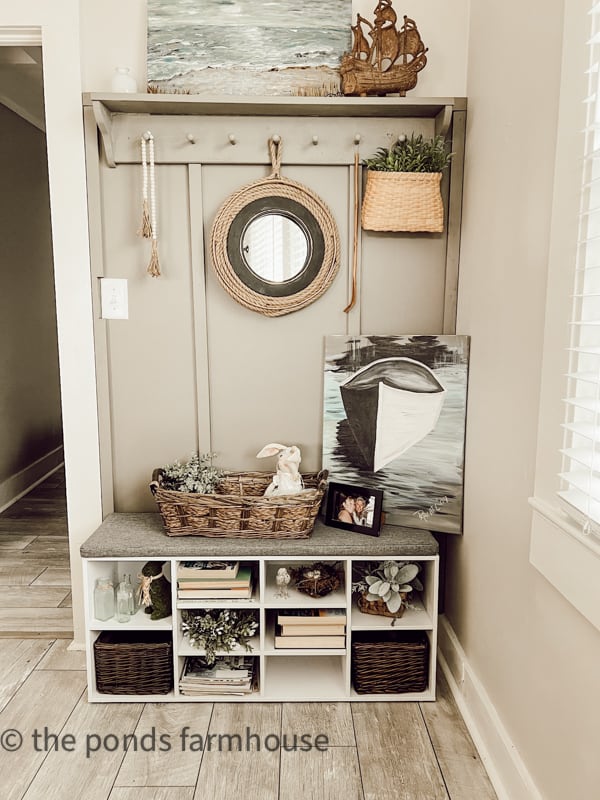 Accent wall in coastal beach cottage with DIY nautical mirror, boat painting and bench with shelving.