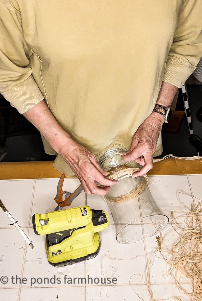 Thrifted Vase with raffia being attached using Ryobi hot glue gun in Pottery Barn hack.