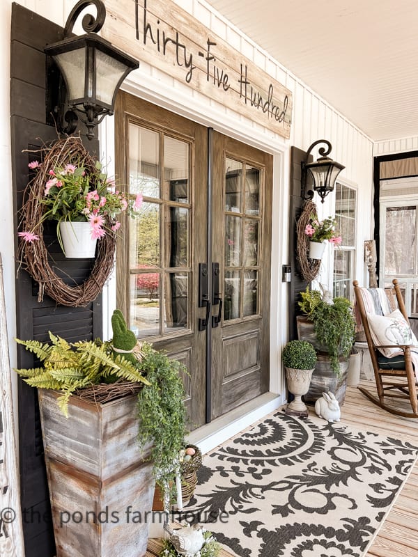 Farmhouse Spring Porch Decor. Side view of large planters with concrete bunny and hanging basket on shutters.