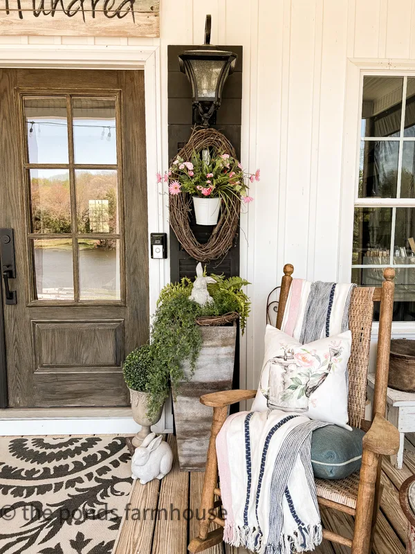 Shutters and planter filled with farmhouse style spring decor. Concrete bunnies. Rocking chair with pillow.