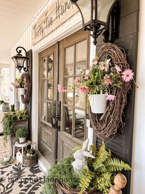 Farmhouse Spring Porch Decor Ideas. Planters, concrete bunnies, wreath with flowers in buckets.