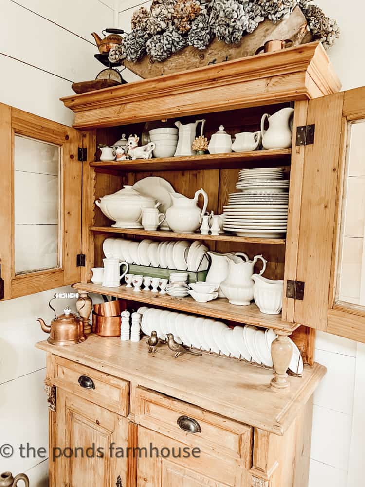 Vintage hutch filled with ironstone, copper and thrift store finds with a honey pine finish and open glass doors