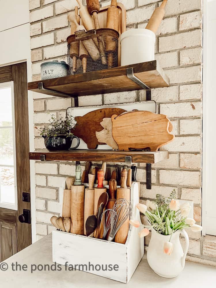 Open Shelving with Vintage Wood cutting Boards & Rolling Pins against a brick wall in industrial farmhouse.