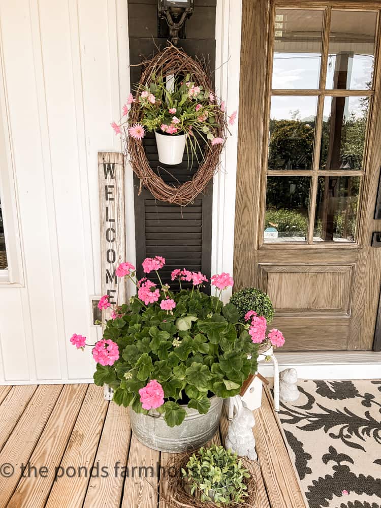 Black shutter beside front door with grapevine wreath and flowers
