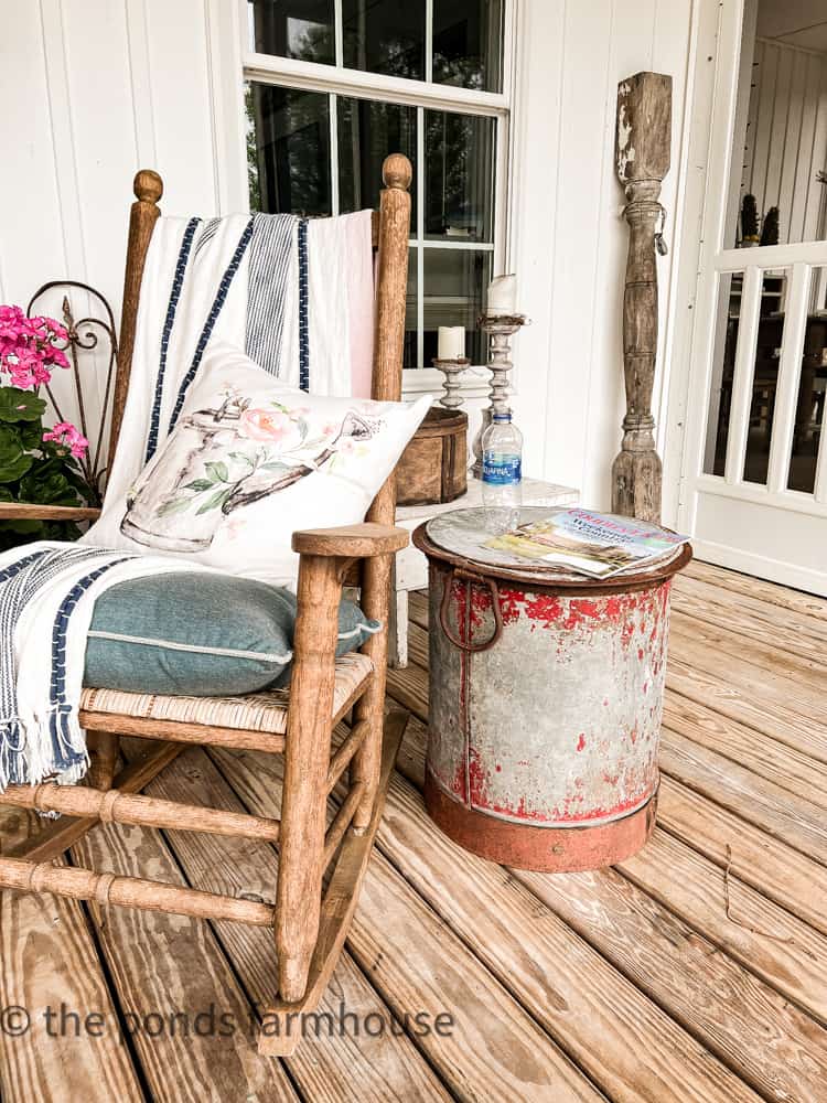 Chippy galvanized bucket serves as a side table on farmhouse porch. Vintage ice bucket decorations.