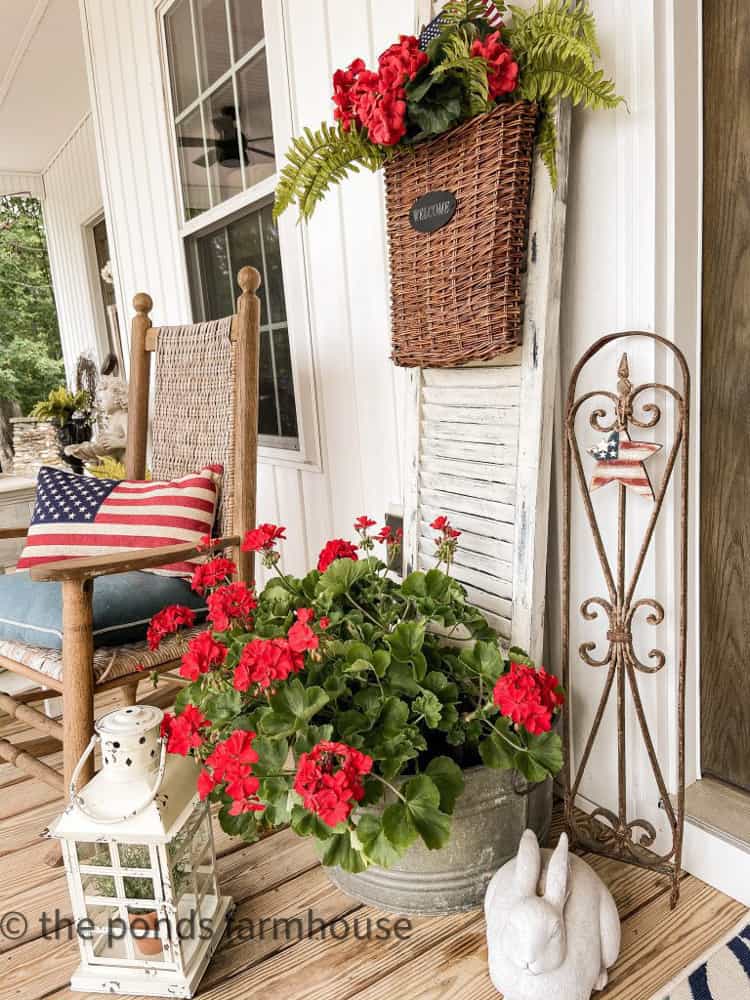 Front Porch Patriotic Decorating with red geraniums in galvanized tub and blue and white rug. Flag Pillow in rocker