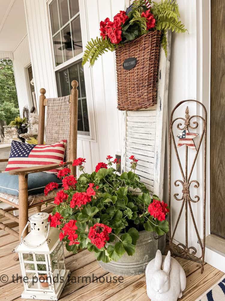 Patriotic pillow on Kennedy rocker beside flowers in galvanized bucket. Concrete bunnies.