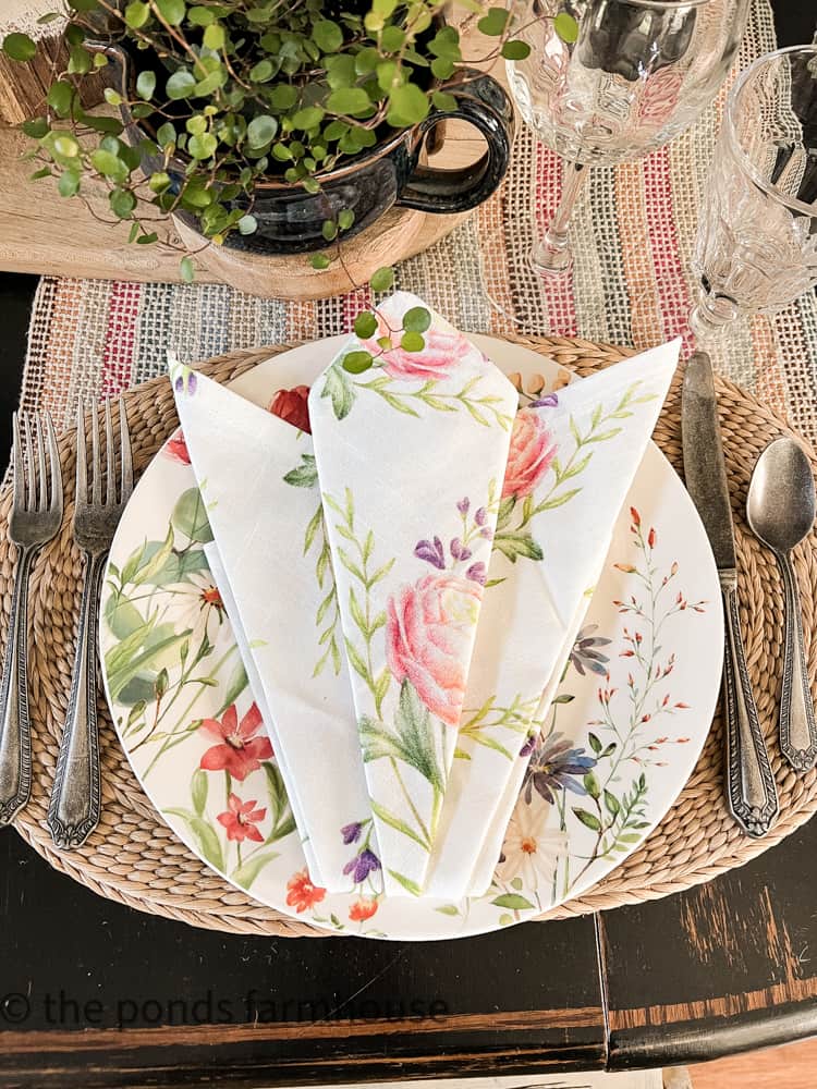 Place setting with folded napkin shaped like a tulip.  Floral Napkins and plates with flowers for festive Summer table.