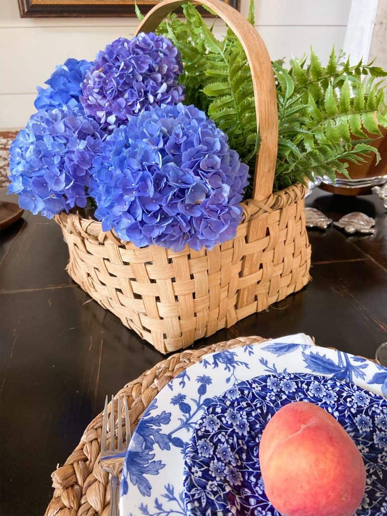 Summer Tablescape Ideas with blue hydrangeas in a basket, woven plate chargers and blue & white dishes