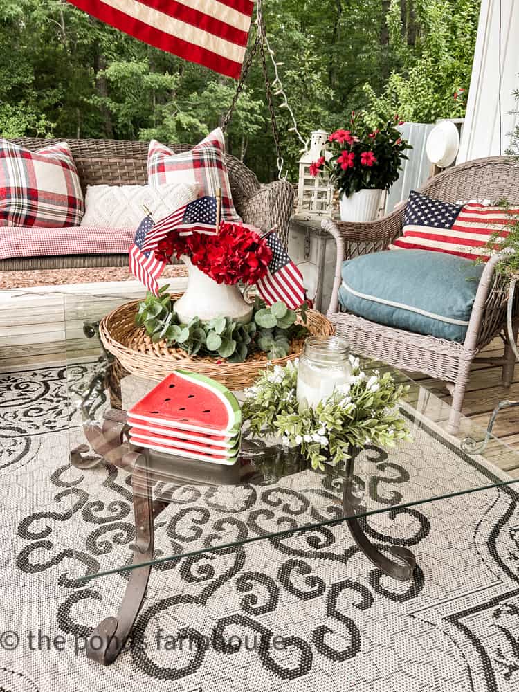 watermelon plates and red geraniums for 4th of July, outdoor rug. Wicker furniture. Outdoor plant decorations.