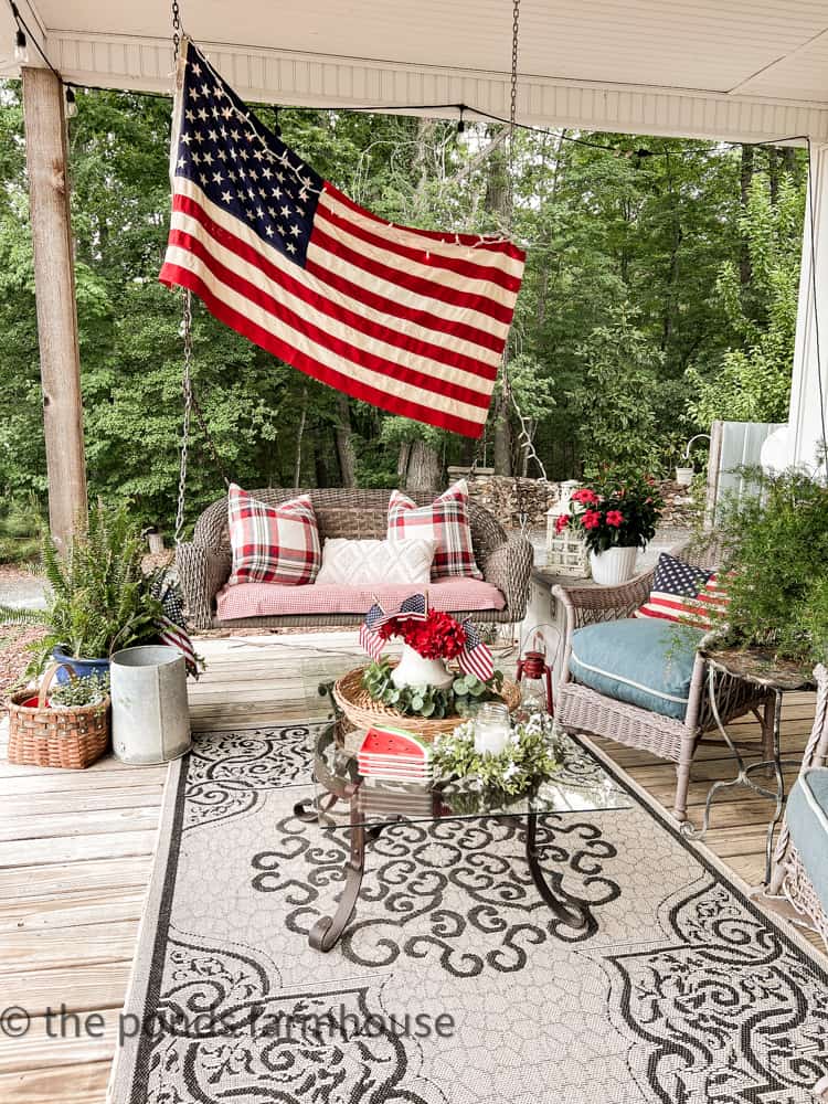 Patriotic Porch Decorations for The 4th of July, patriotic pillow. Wicker porch swing and chairs. Outdoor rug.