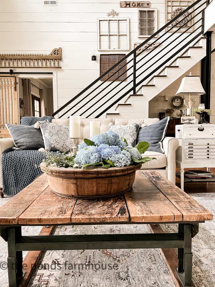 Wooden bowl filled with blue hydrangeas add shades of blues colors. Blue pillow on sofa.