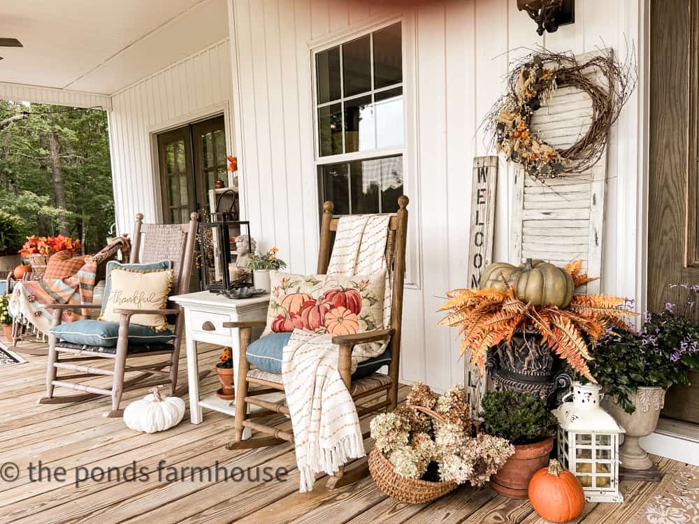 Cozy seating area for large front porch ideas with planters filled with pumpkin, basket of dried hydrangeas and throw pillows