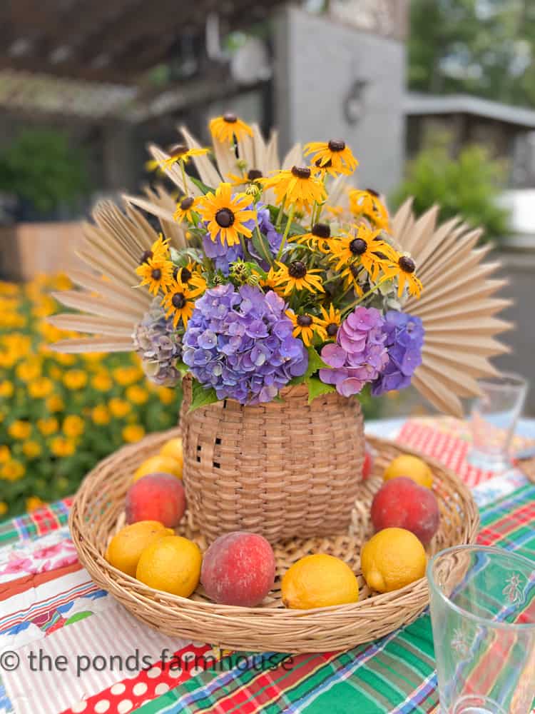 Free Centerpiece basket filled with fresh hydrangeas, black eyed susans, dried palm leaves surrounded by fruit. 