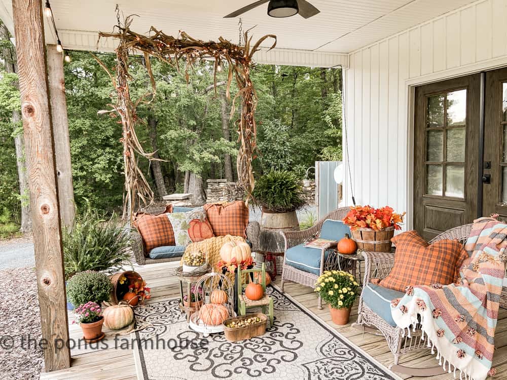 Farmhouse front porch ideas with porch swing and corn stalk garland with cozy throw pillows & pumpkins