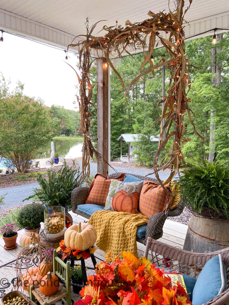 Porch Swing on Farmhouse Fall Porch Tour with corn shucks and pillows and throw blankets with view of ponds.