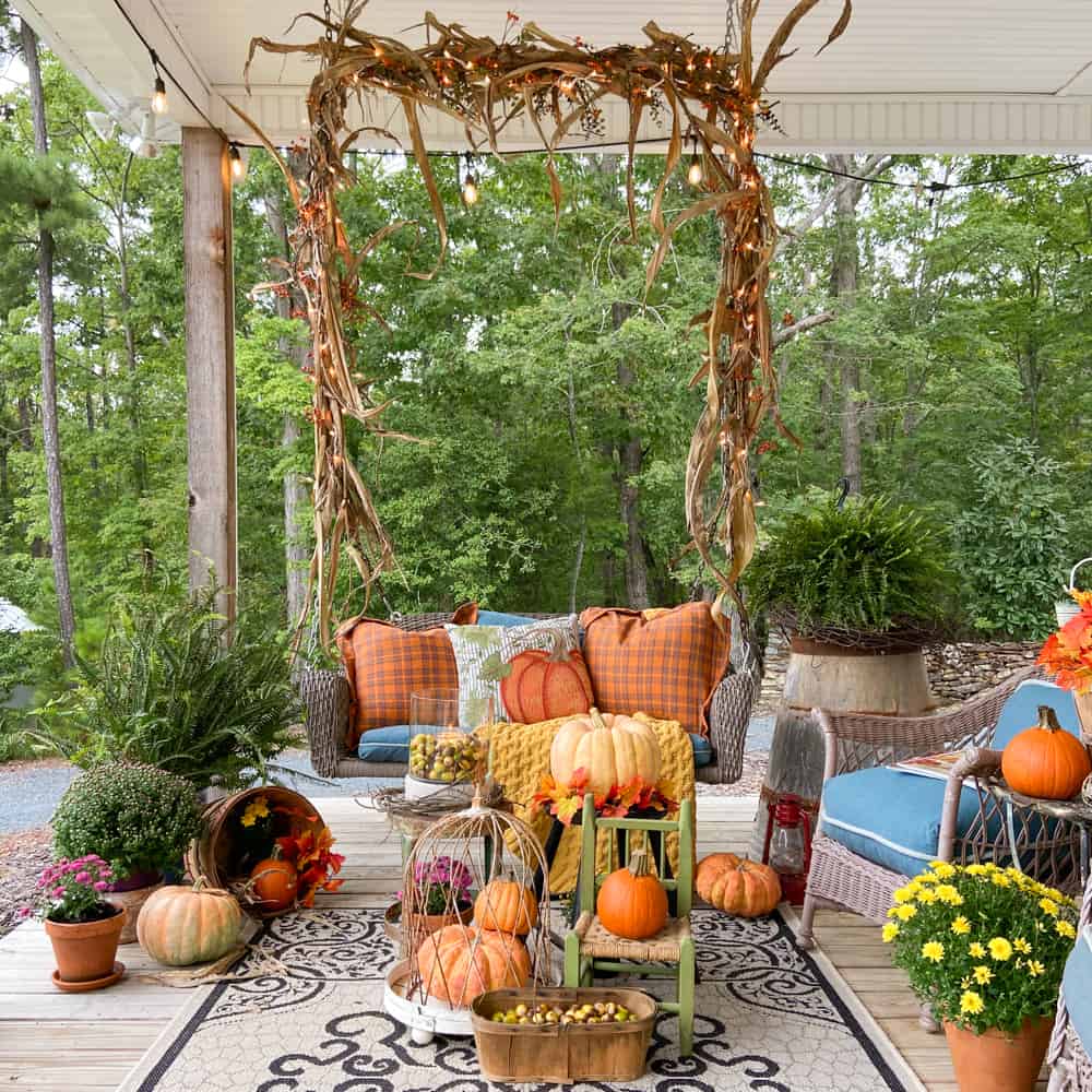 Front porch swing with corn shucks, pumpkins, mums, throw pillows and throw blankets.  Fern and wicker rockers.  