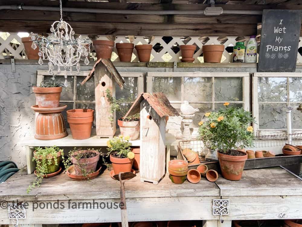 DIY Potting Bench hold thrifted terra cotta and clay pots.  A vintage chandelier with solar light strand hangs from above.  